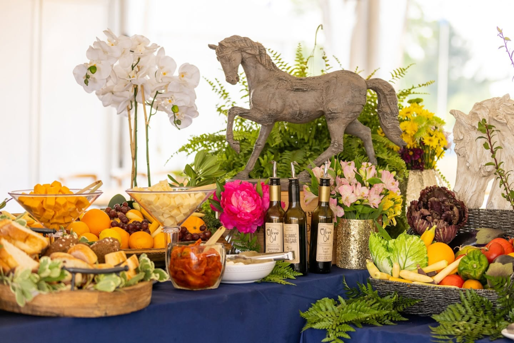 Table with horse sculpture and flowers along with breads, cheese, fruit and vegetables.