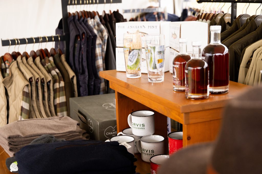 Shelf with mugs, glasses, and bottles set between racks of clothing.